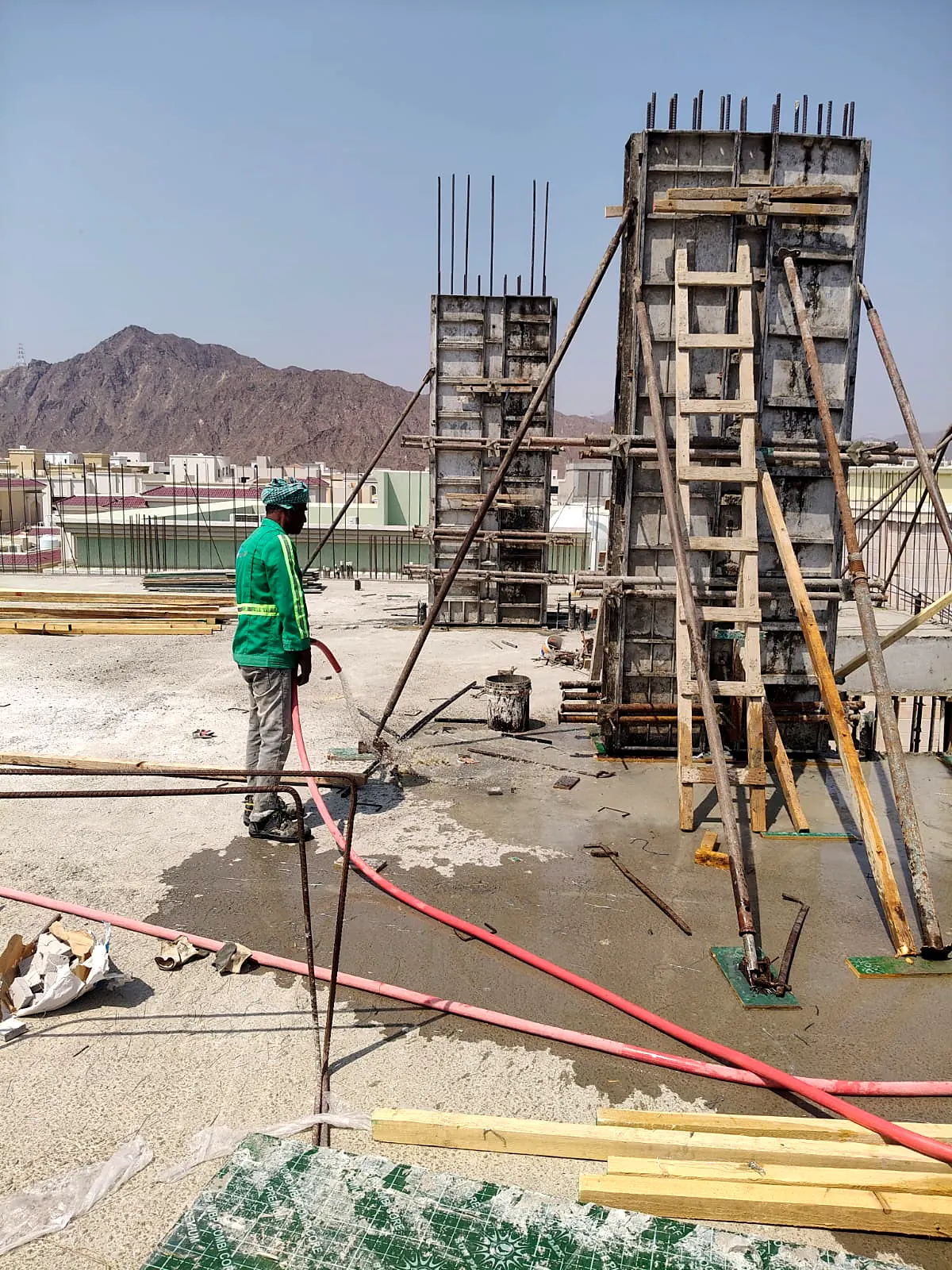 Workers bracing column formwork on a villa roof slab with the Khorfakkan mountains behind