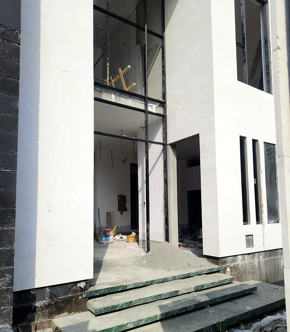 Double-height glazed entrance of a white villa with dark stone steps under construction