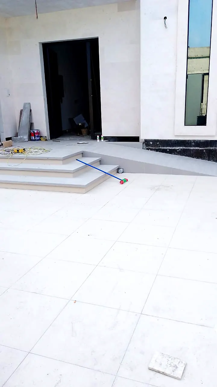 Large-format white tiles laid at an external entrance with dark stone steps