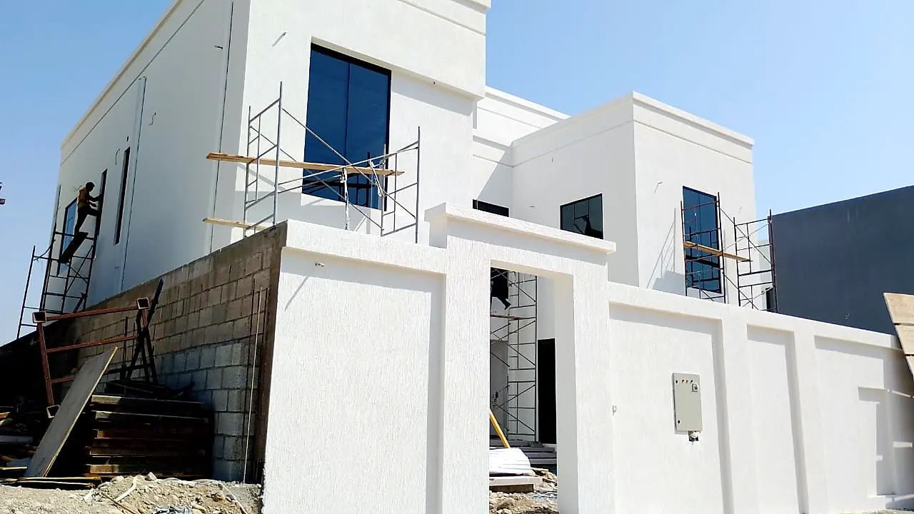 White villa with parapet walls and boundary wall during finishing works, scaffolding in place
